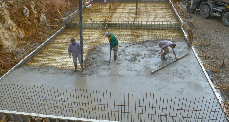 Construction workers pouring and smoothing concrete to create a solid foundation for a building, surrounded by rebar and scaffolding.