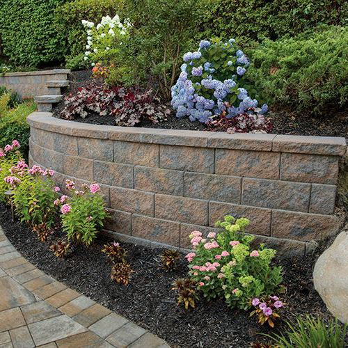 A decorative retaining wall in a garden setting with a variety of colorful flowers and plants, demonstrating practical yet attractive landscaping solutions.