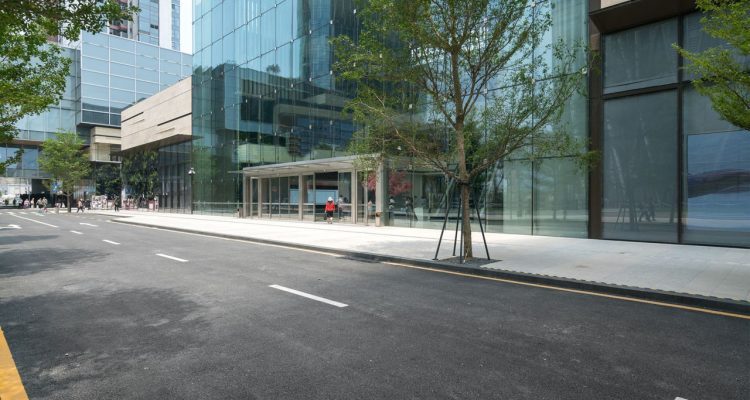 A contemporary urban streetscape featuring wide concrete sidewalks and a glass-fronted building, showcasing modern city planning and pedestrian-friendly design.