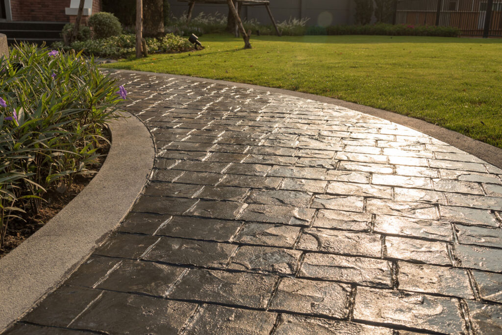 A curved stamped concrete pathway featuring a sleek design, complemented by vibrant greenery and flowers.